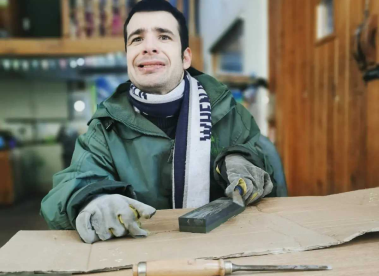 An Earthworker holding a piece of file sat at a work table, wearing protective gloves