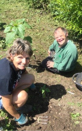 One Earthworker and one Volunteer working together in the garden, using hand forks and wearing gardening gloves