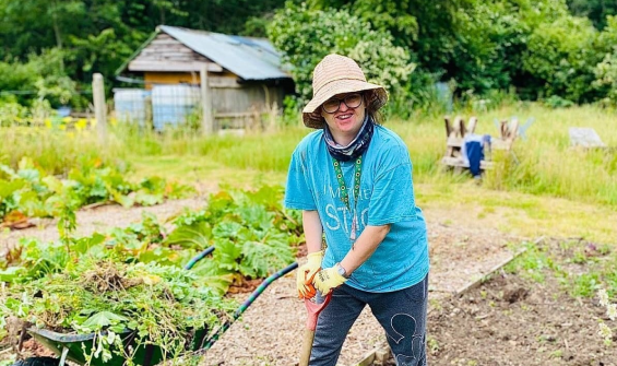 An Earthworker standing in a planting bed, leaning over a shovel whilst digging