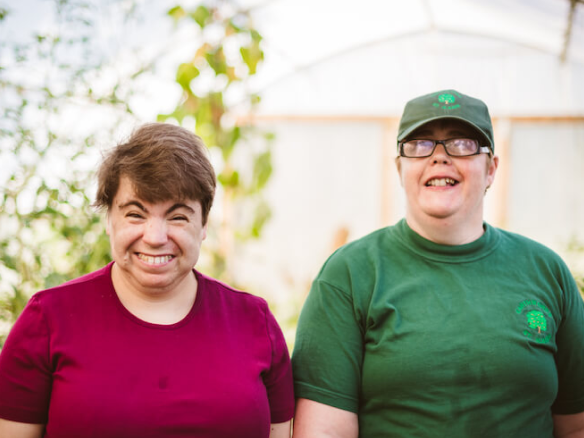 Two Earthworkers stood next to each other smiling in the polytunnel