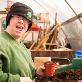 An Earthworker smiling whilst potting a plant in the greenhouse.