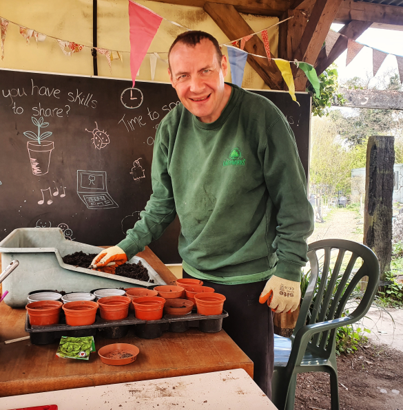 An Earthworker smiling and potting some small plants inside