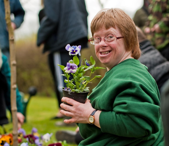 An Earthworker sat smiling, holding a small plant with purple flowers
