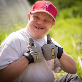 An Earthworker smiling with their thumbs up, wearing gardening gloves