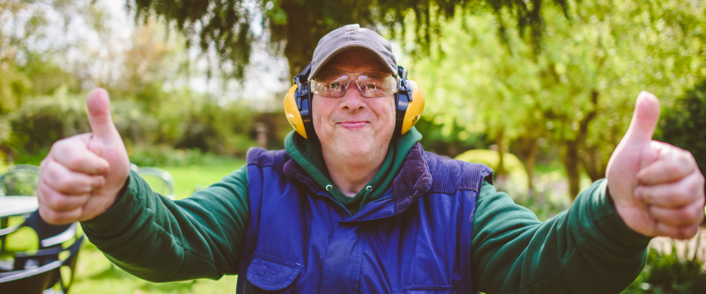 An Earthworker holding both thumbs up to the camera, wearing ear defenders and safety glasses