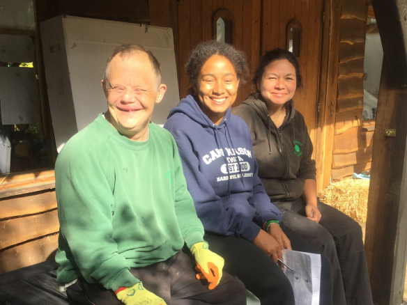 An Earthworker, support worker and staff member, sat together outside The Warren in the sunshine, taking their morning break