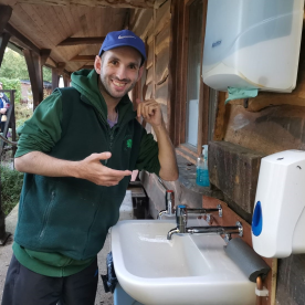 An Earthworker is smiling next to a hand washing station outside