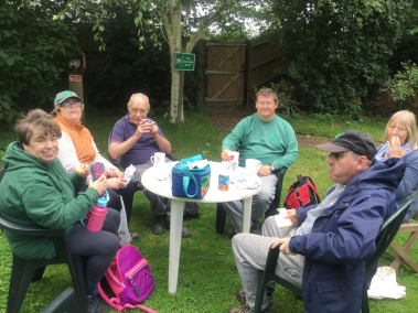 A group of six Earthworkers and Volunteers sitting around a garden table taking a lunch break