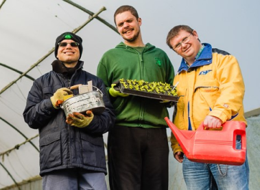 A group of 3 Earthworkers standing together holding various pieces of gardening equipment