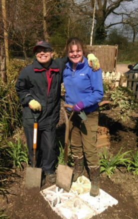 An Earthworker and a Volunteer standing arm-in-arm, holding shovels