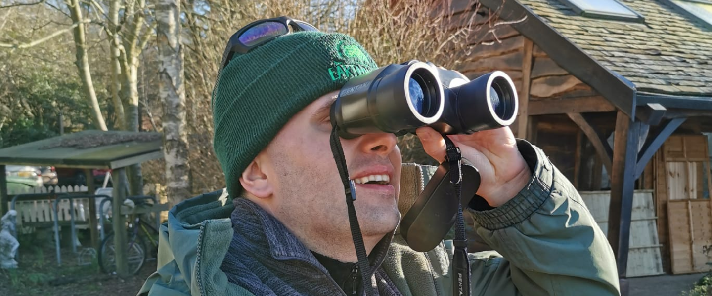An Earthworker in the gardens looking through a pair of binoculars