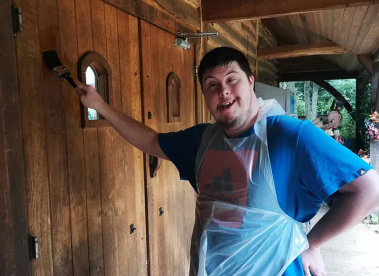 An Earthworker using a paintbrush to paint a wooden door, wearing apron