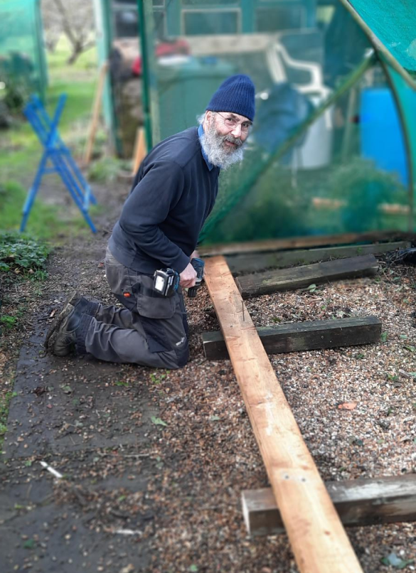 A volunteer using a screwdriver to assemble pieces of wood, whilst kneeling to the ground