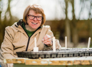 An Earthworker smiling, with a tray of potted plants in front of her