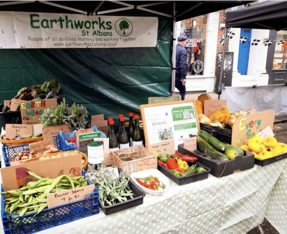 Alt text: A view of an Earthworks stand at a Farmers Market, displaying fresh fruit and vegetables amongst other produce