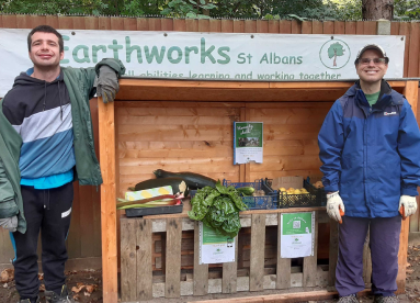 Two Earthworkers standing in front of the Farmers Market fruit and vegetable stall