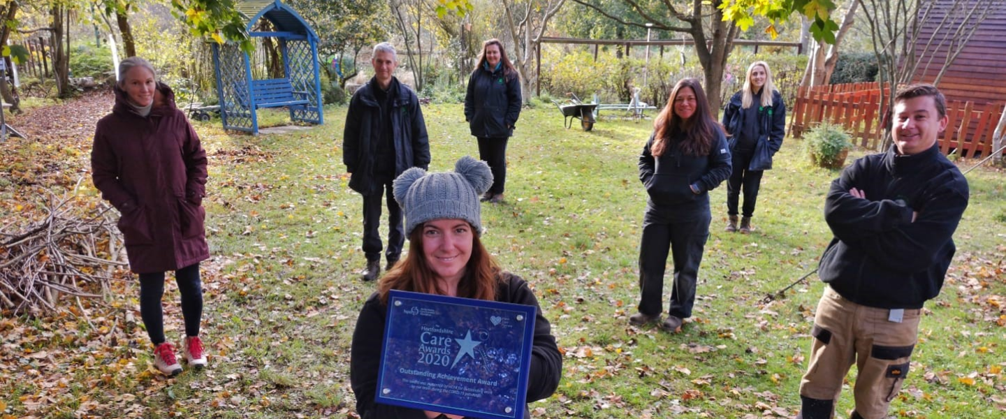 Our staff members team in the garden, holding up the Hertfordshire Care Award Outstanding Achievement Award 2020