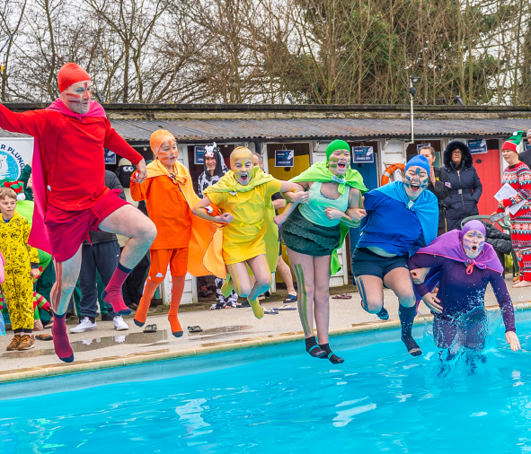 Six of the St Albans community in colourful costumes and capes, jumping into a cold outdoor pool, for the Polar Bear Plunge event