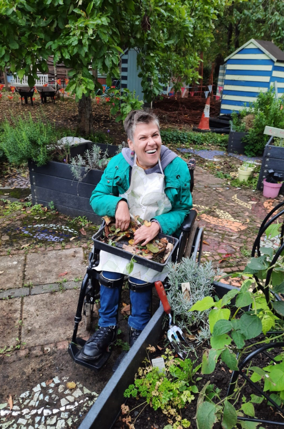 An Earthworker in a wheelchair, holding a tray of gardening materials