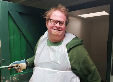 An Earthworker walking out of a green wooden door, wearing a plastic apron and protective gloves