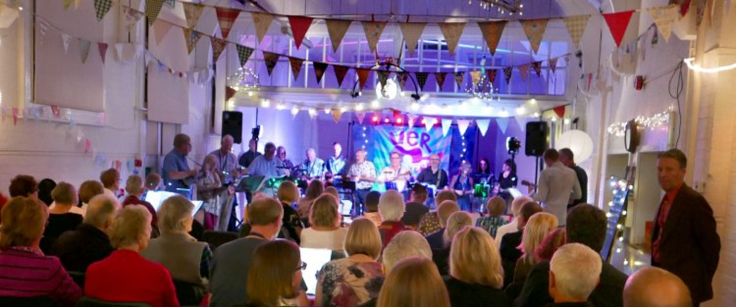 A crowded concert hall at a charity event, a large stage ahead decorated with bunting